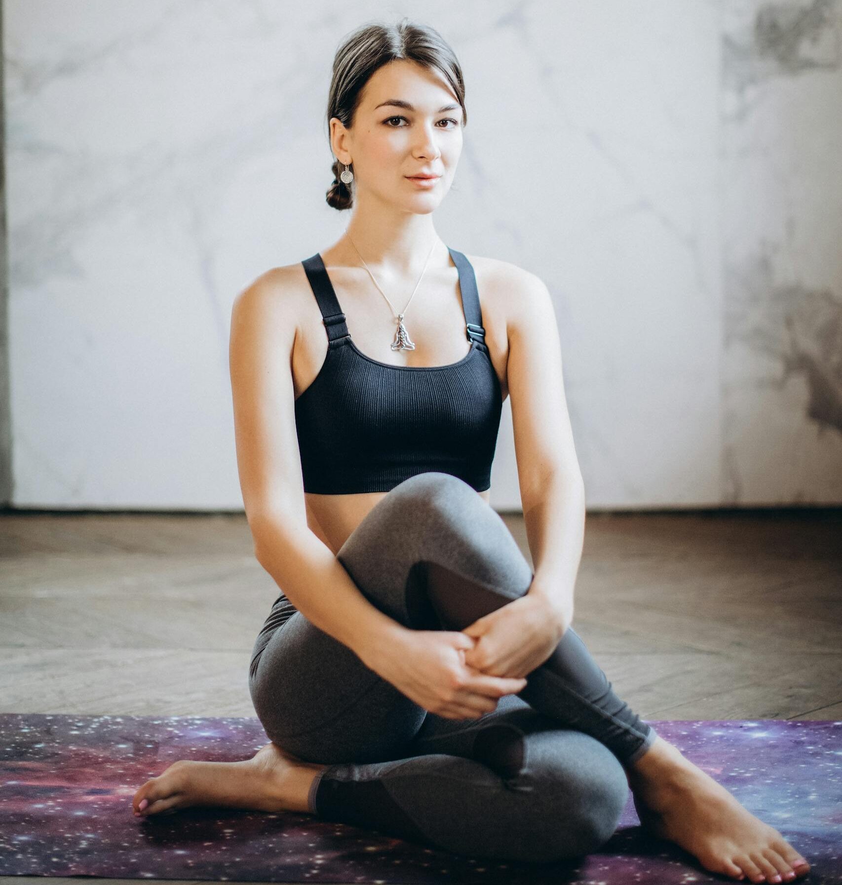 A woman in activewear sitting in a yoga pose indoors, promoting fitness and mindfulness.